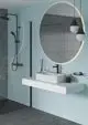 Duschsystem von Ideal Standard mit schwarzem Handbrausekopf und minimalistischer Wandmontage. Unauffällige Armatur über Waschtisch mit Glasscheibe und beleuchtetem Spiegel.